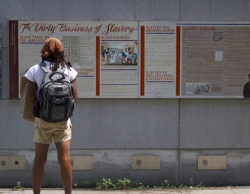 A visitor at Independence National Historical Park stands in front of an exhibit reading The Dirty Business of Slavery