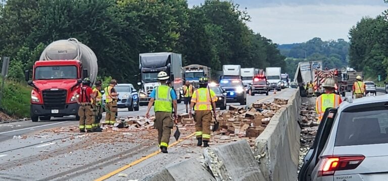 Firefighters work to clean up hot dogs spilled from a truck on a highly traveled interstate