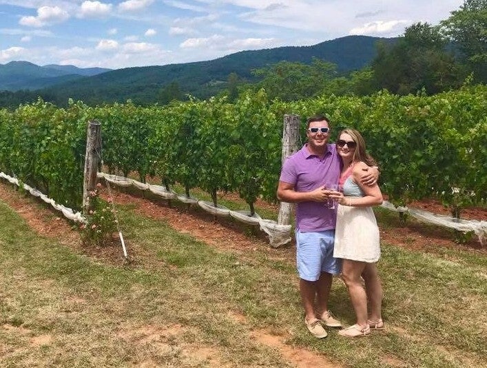 A man and a woman side hug while sharing a glass of wine at a winery
