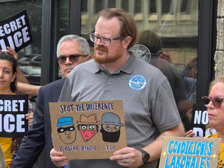 Danny Bauder holds a sign criticizing ICE agents for wearing masks