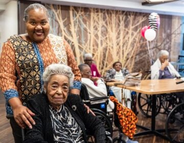 A woman standing behind her elderly aunt who is sitting in a wheelchair
