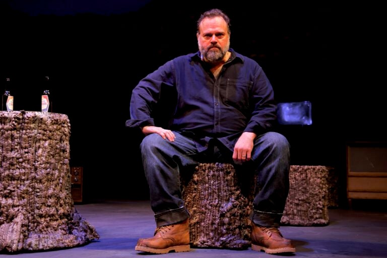A man sitting down in a scene from the play