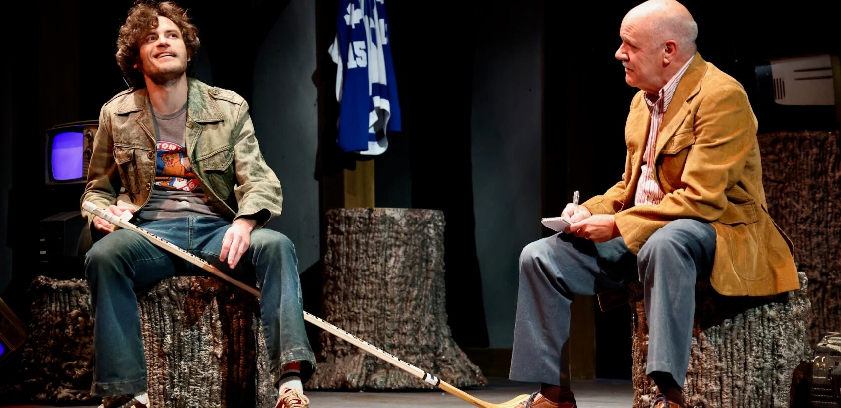 Two men talking while stiting down. One of them is holding a hockey stick