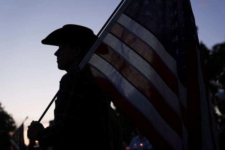 Charlie Kirk Shot A silhouette of a man wearing a cowboy hat holding a large American flag