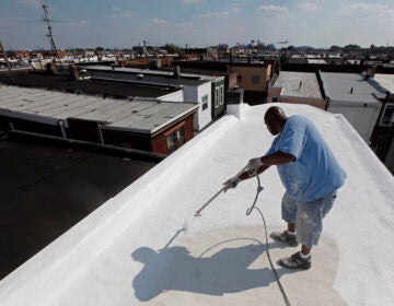 a worker applies a coating of Acrymax to the roof of a rowhouse in Philadelphia