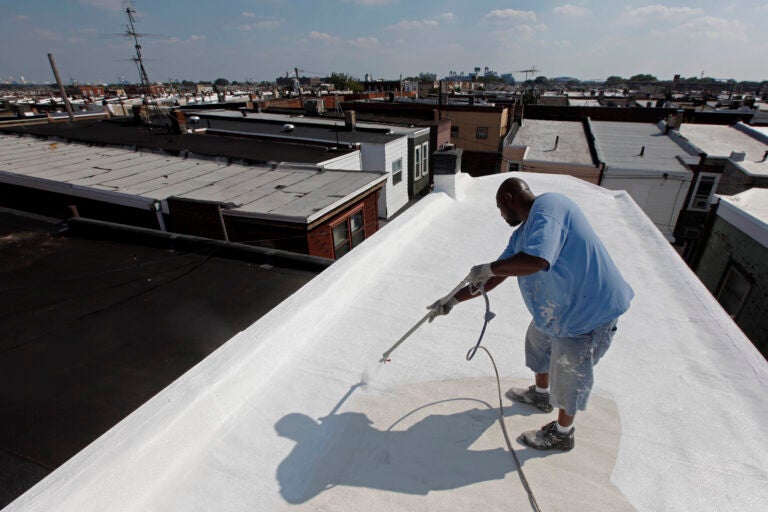 a worker applies a coating of Acrymax to the roof of a rowhouse in Philadelphia