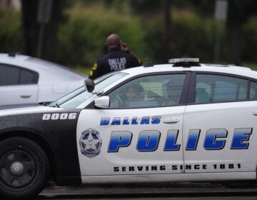 An officer stands behind a Dallas Police Department car in the middle of the street