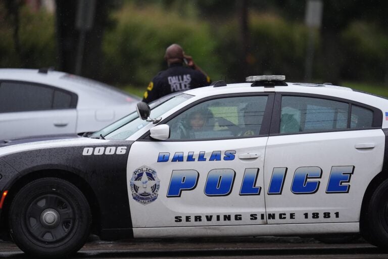 An officer stands behind a Dallas Police Department car in the middle of the street
