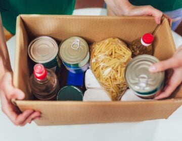Someone holds a cardboard box filled with nonperishable food