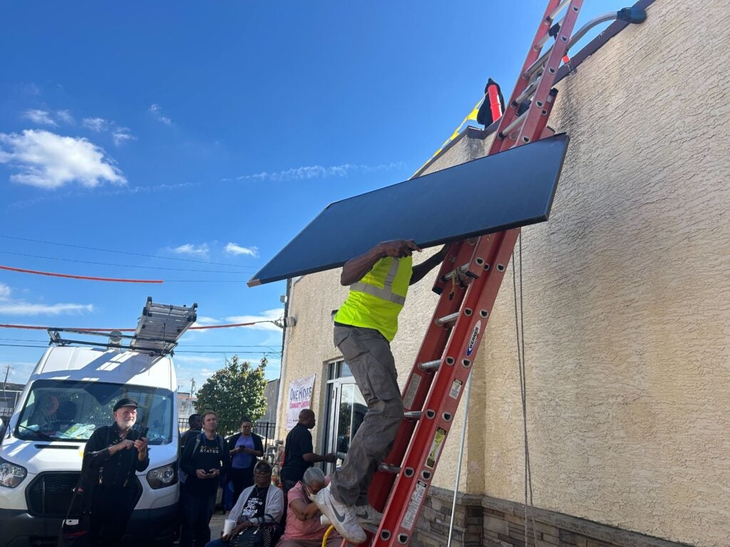 A solar installer carries a panel down from the roof of One Hope Community Church in Hunting Park.