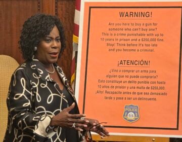Mayor Cherelle Parker next to a board reading, in Spanish and English, WARNING! Are you here to buy a gun for someone who can't buy one? This is a crime punishable with up to 10 years in prison and a $250,000 fine. Stop! Think before it's too late and you become a criminal.