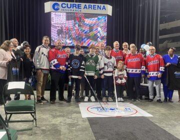 Officials posingwith youth hockey players wearing their jerseys and holding hockey sticks