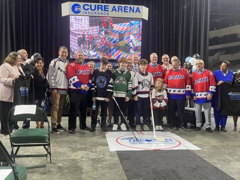 Officials posingwith youth hockey players wearing their jerseys and holding hockey sticks
