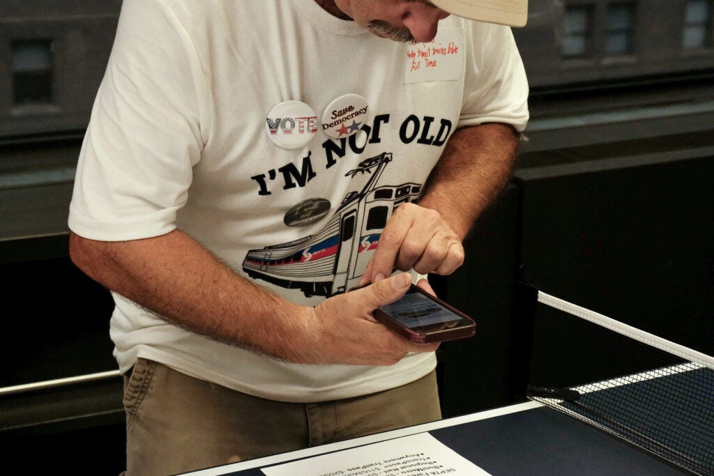 A man is leaning in to take a cell phone photo of a document on a table.