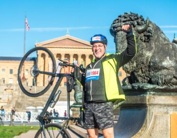 A man raising his fist and holding up his bike in front of the Art Museum steps