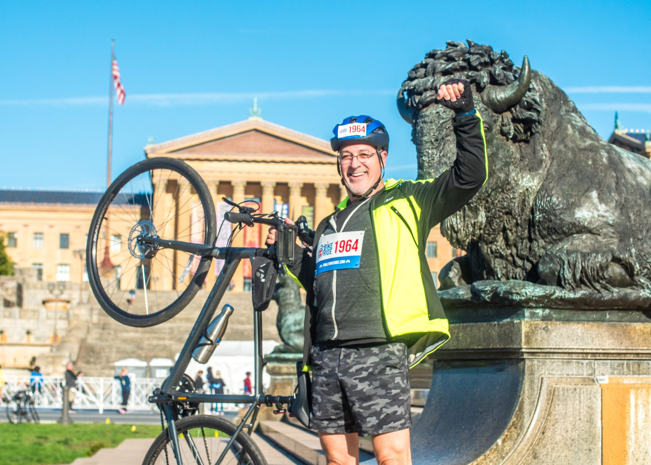 A man raising his fist and holding up his bike in front of the Art Museum steps