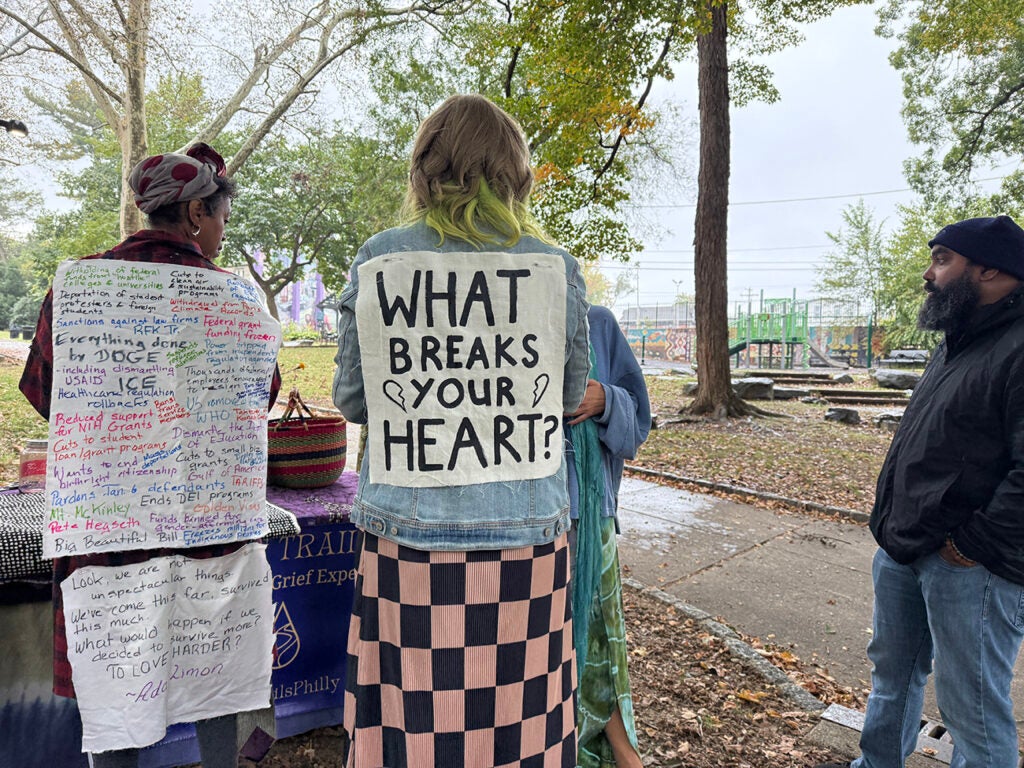 A woman wears a sign on her back that reads "What breaks your heart?"