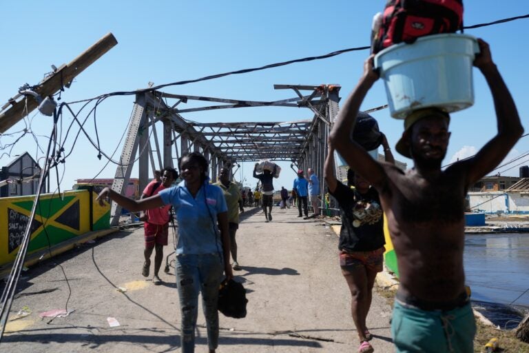 hurricane-melissa-jamaica-2025-10-30 Residents leaving Black River, Jamaica with a damaged bridge behind them
