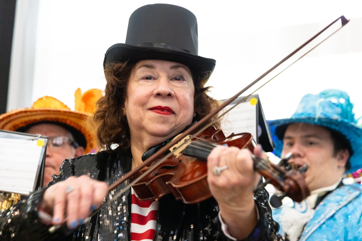 A woman wearing a top hat places the violin