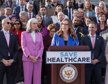 Government Shutdown Sarah McBride speaking at a podium surrounded by fellow Democrats