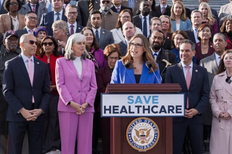 Sarah McBride speaking at a podium surrounded by fellow Democrats
