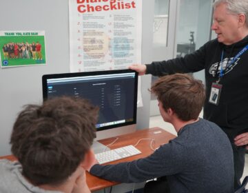 A teacher looking intently at a computer monitor with two students