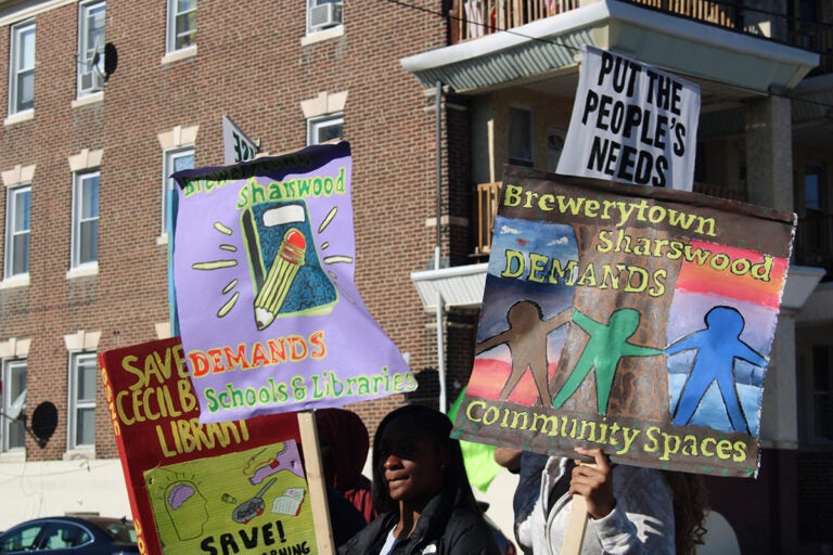 People hold signs while marching in the 25th annual Peoplehood Parade in West Philadelphia