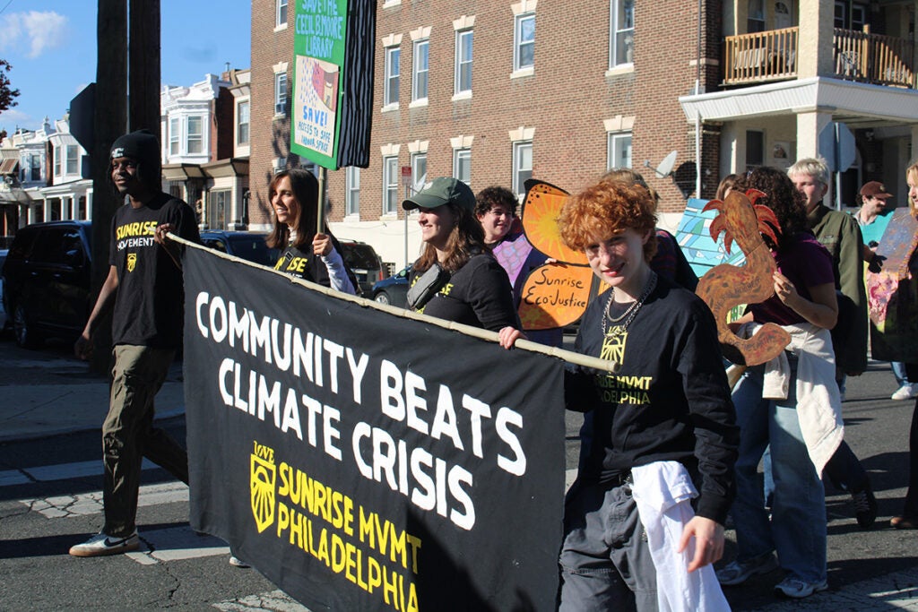 People hold a sign that reads "Community Beats Climate Crisis" in the 25th annual Peoplehood Parade in West Philadelphia
