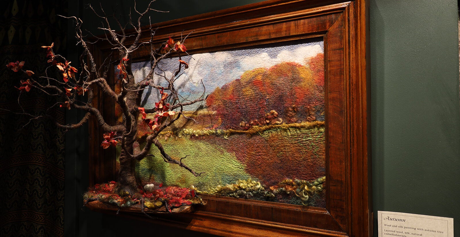 A landscape painting sits behind a small tree on display
