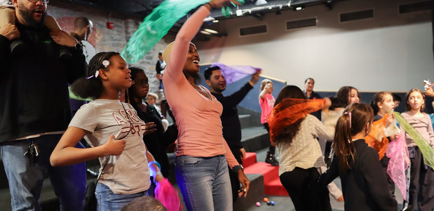 Children and parents raise ribbons above their heads as they dance to music