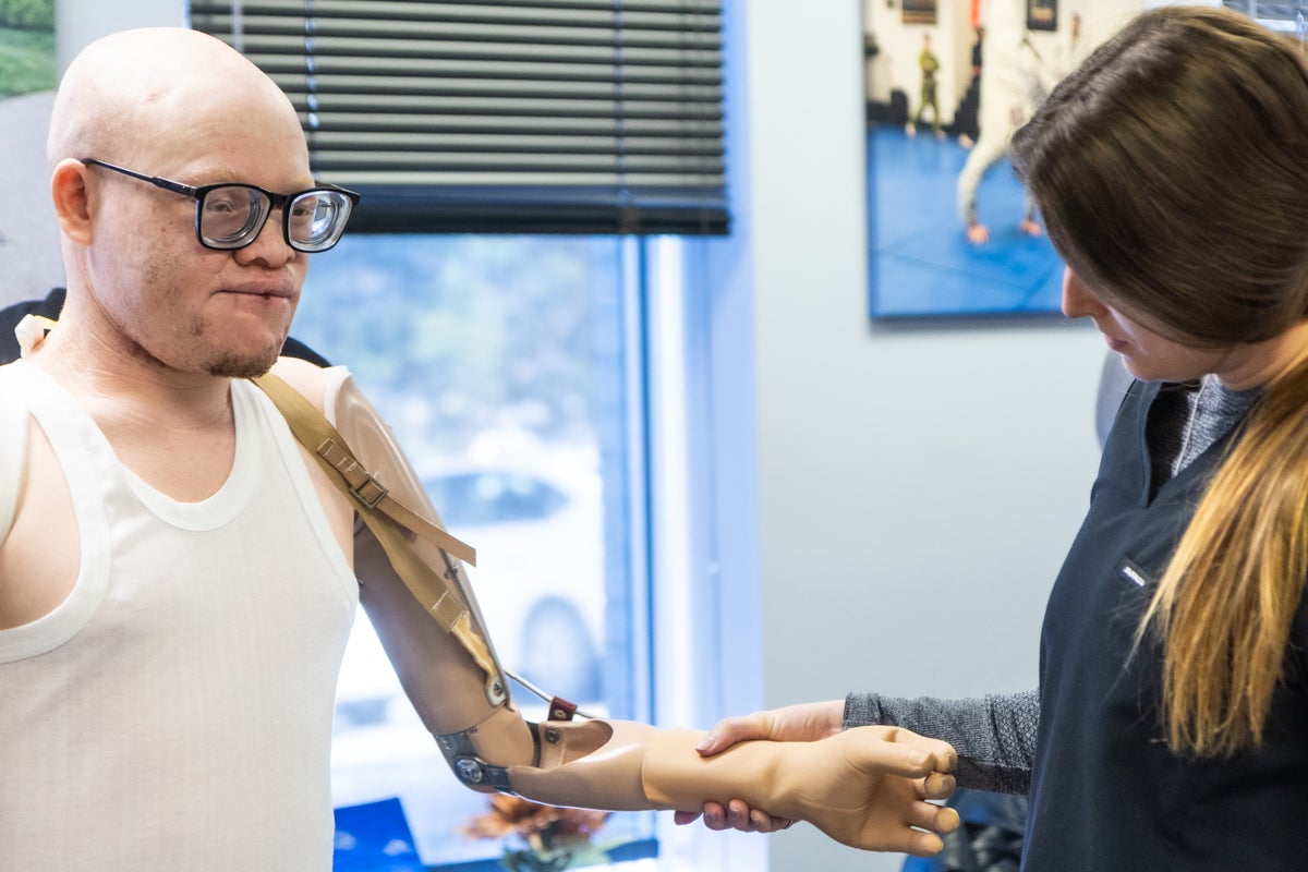 A nurse is holding Emmanuel's prosthetic left arm, as they work on exercises together