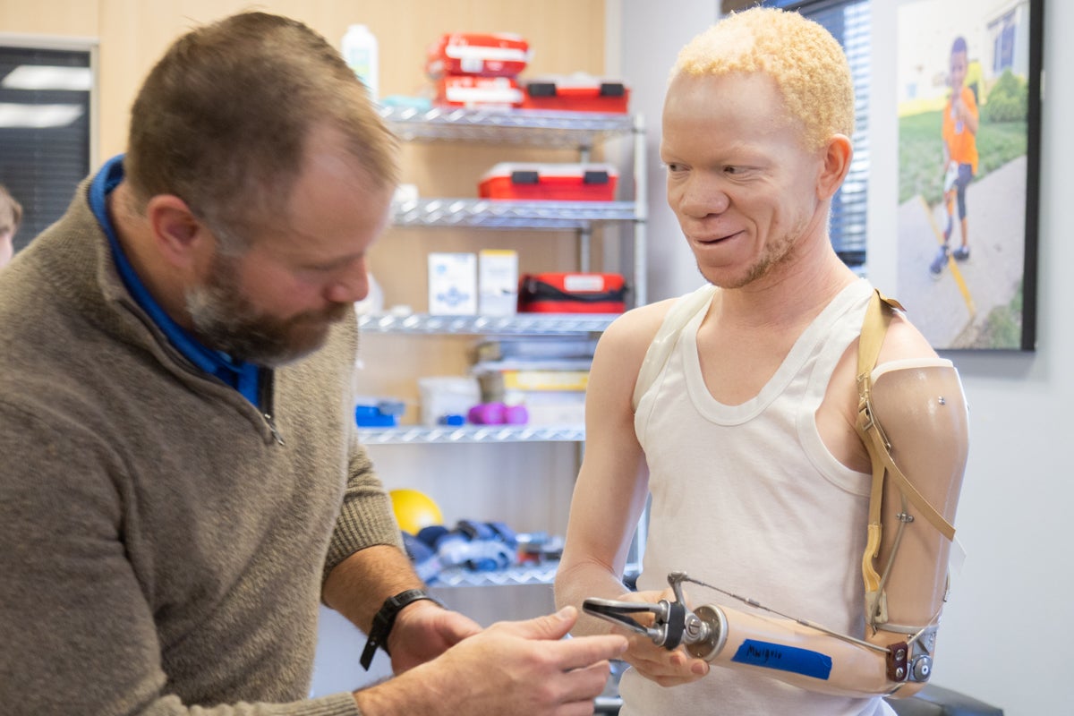 A doctor closely examines the prosthetic left arm of Mwigulu, who is smiling