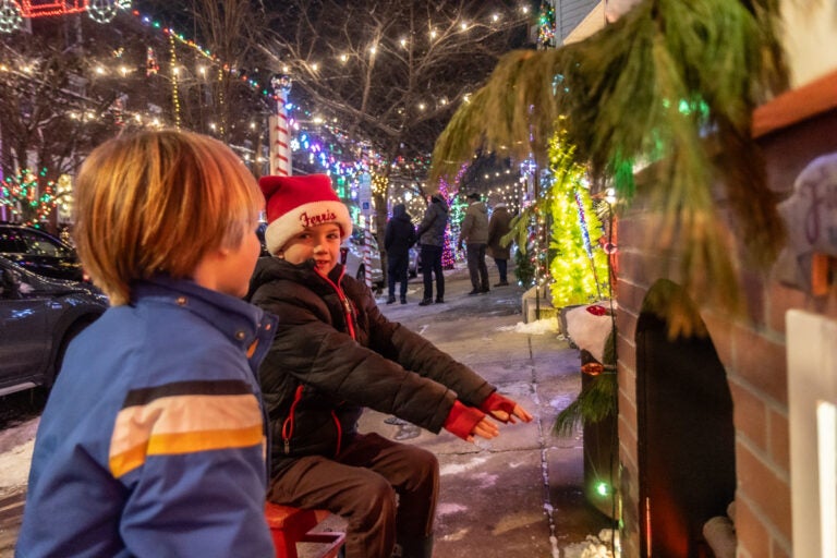Two children extend their hands toward an artificial fireplace at the Miracle on South 13th Street light display in South Philadelphia