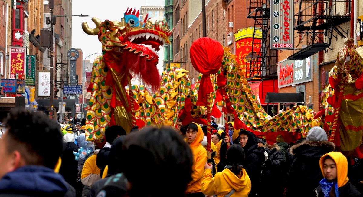 People holding up a long flying dragon while marching down the street as part of the Lunar New Year parade in Philadelphia's Chinatown.
