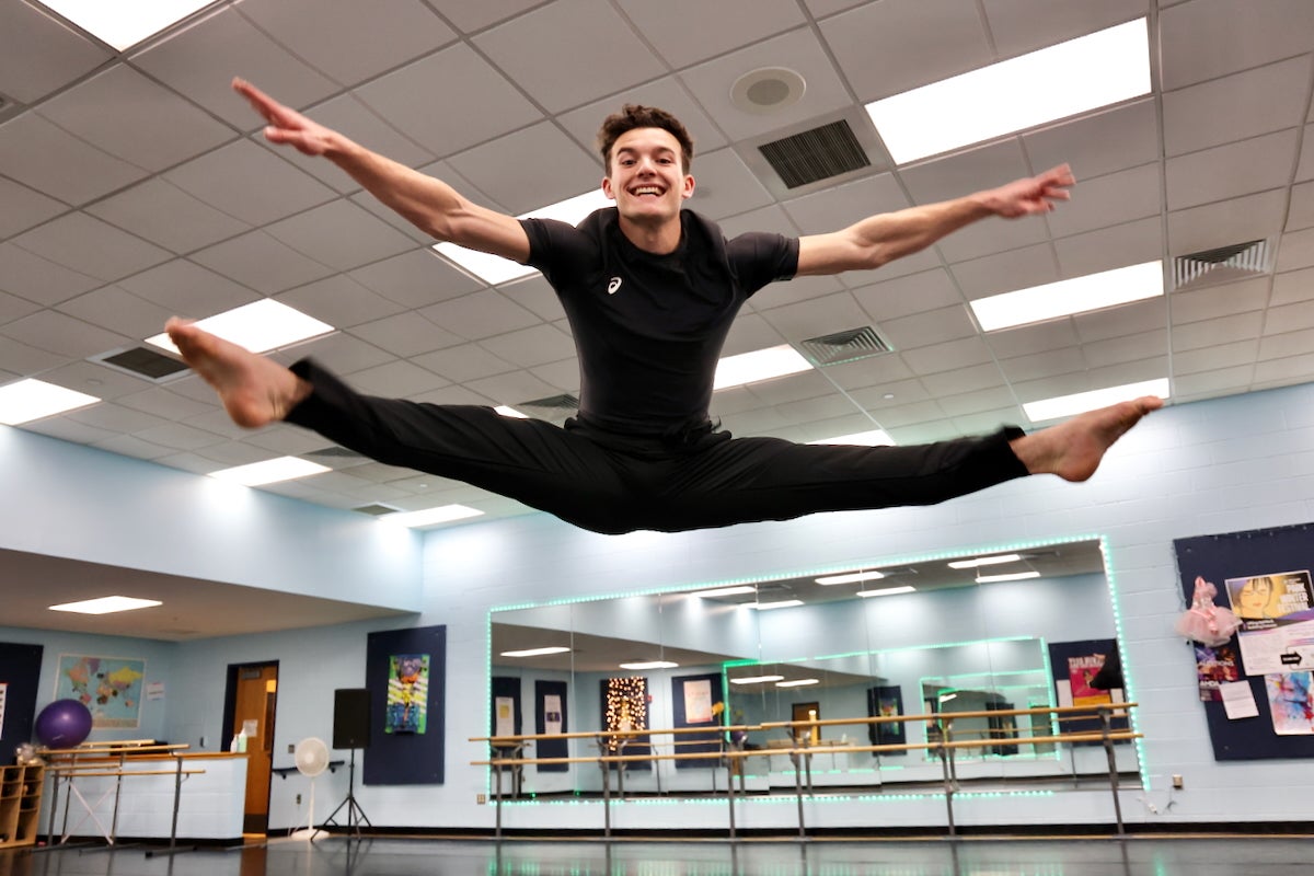 Stephen Tetkowski is smiling as he jumps in the air and does a split with his arms stretched out inside the ballet studio at the Arts Academy of Benjamin Rush in Philadelphia.