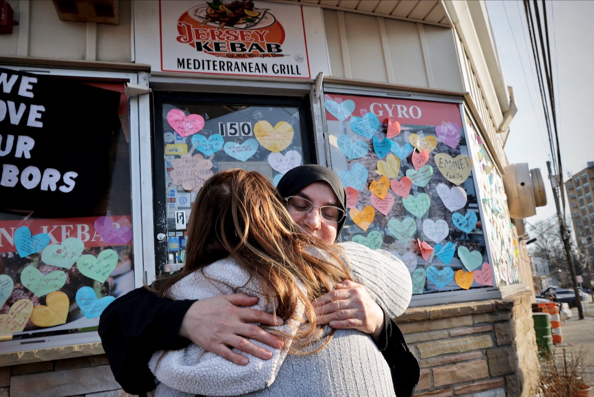 Emine Emanet gets a hug from a neighbor in front of her family’s restaurant, Jersey Kebab, in Haddonfield Township, New Jersey, on March 14, 2025. The restaurant's windows are covered with heart-shaped messages of support from the community.