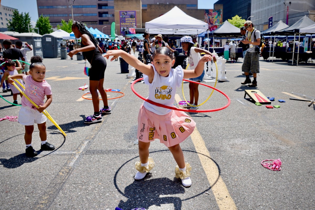 5-year-old Nini Garrett and several other children are hula-hooping at the Juneteenth Block Party put on by the African American Museum in a large parking lot in Philadelphia on June 19, 2025.