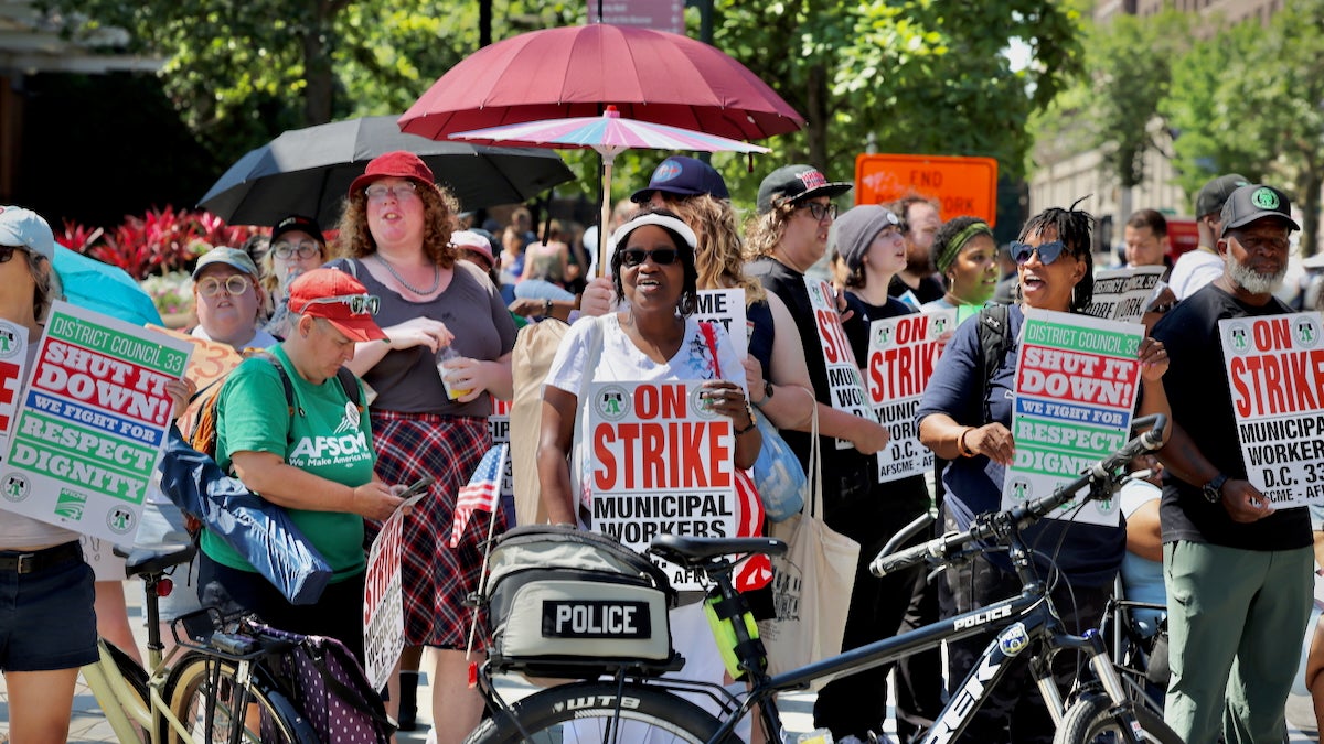 A large group of Philadelphia municipal workers is holding signs reading 'On Strike' as they march down the street along the route of the 4th of July parade in Center City.