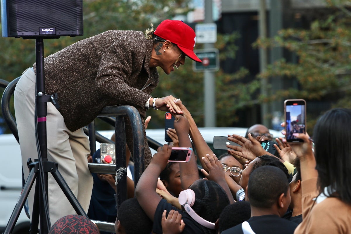 WNBA champion and Unrivaled athlete Natasha Cloud is on stage in Philadelphia's LOVE Park, smiling and reaching down to shake hands with a large group of enthusiastic fans in the audience.