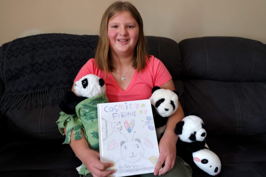 A 10-year-old girl sits on a couch while surrounded by stuffed panda toys