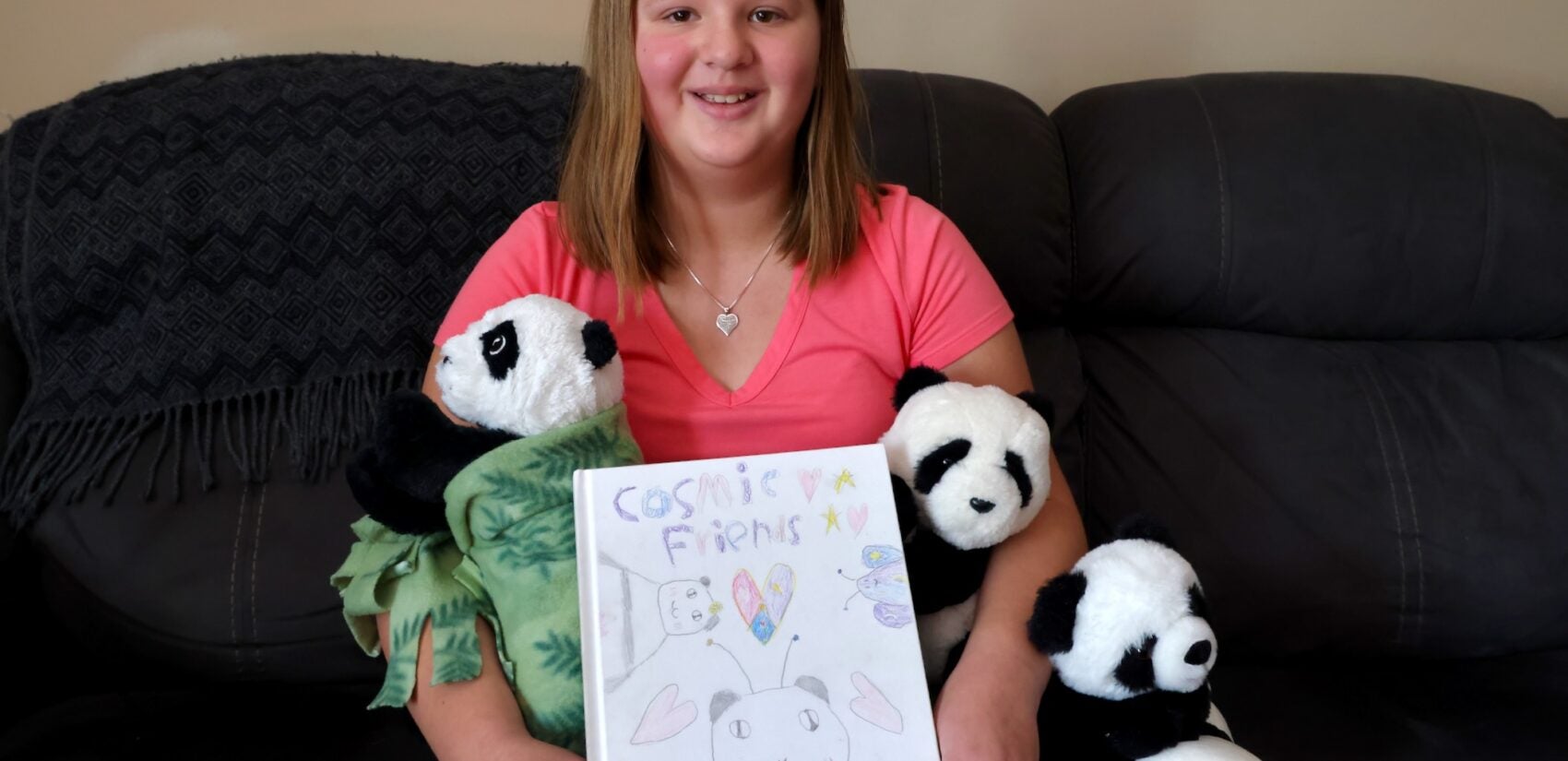 A 10-year-old girl sits on a couch while surrounded by stuffed panda toys