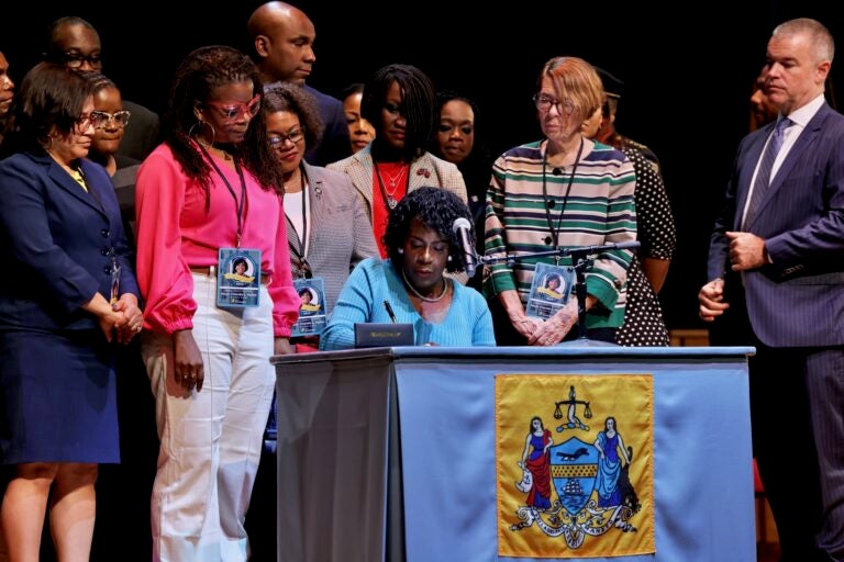 Cherelle Parker sitting at a table signing an executive order as she is surrounded by supporters