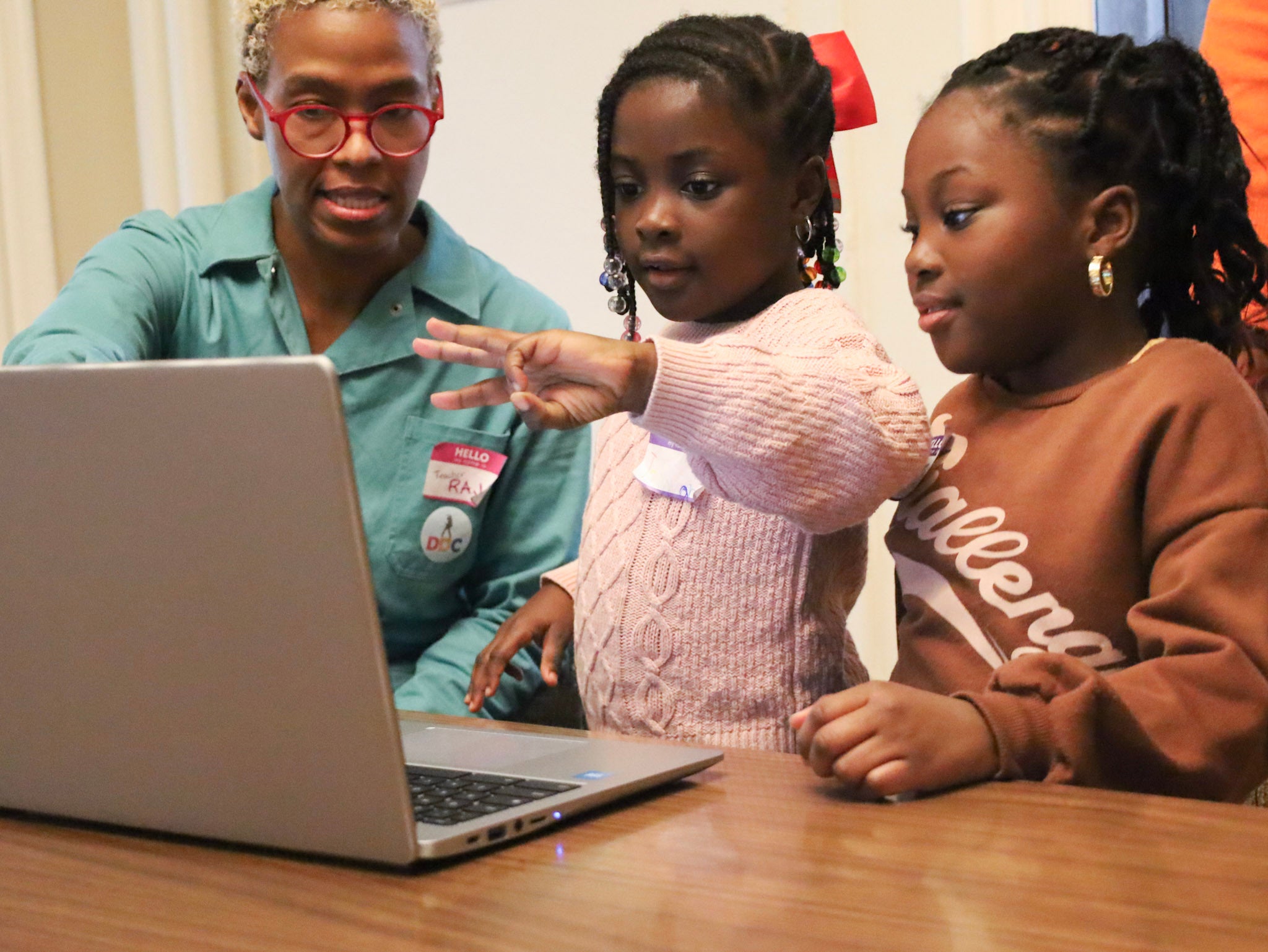 a Drexel professor assists a child holding up a hand pose in front of a webcam