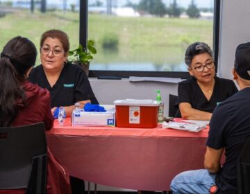 the Mexican Consulate in Oklahoma City Assistant Leticia Orozco, left, and Dr. Carmen Romo, right, talk to clients while testing them for signs of diabetes during a health fair on June 6, 2025, at the Mexican Consulate in Oklahoma City. (Lionel Ramos/ KOSU)