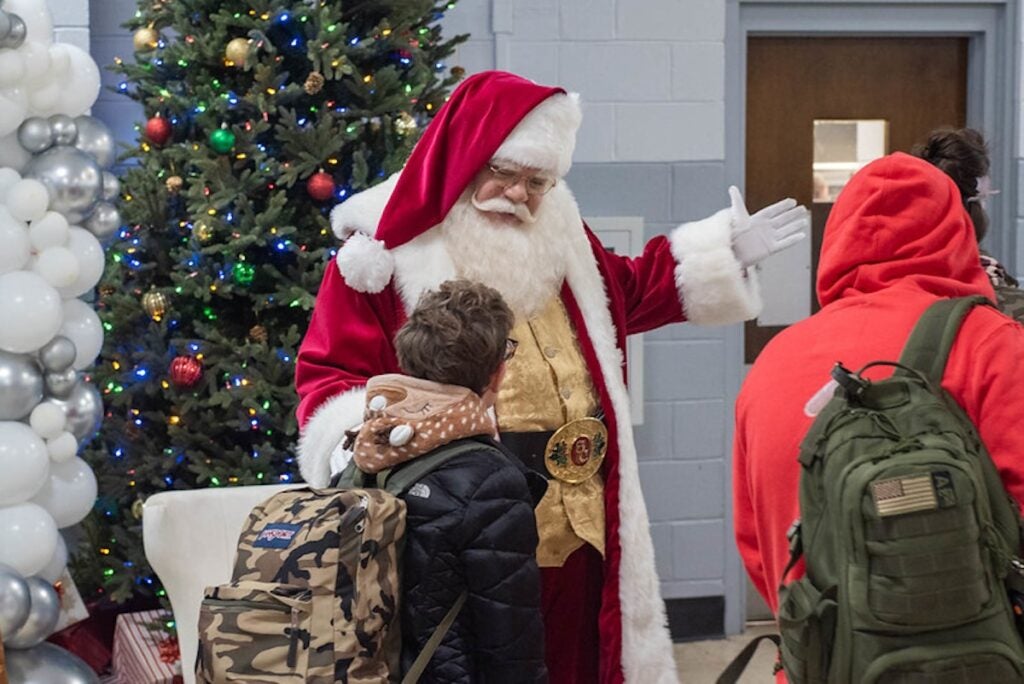 A person dressed as Santa greets two children wearing backpacks