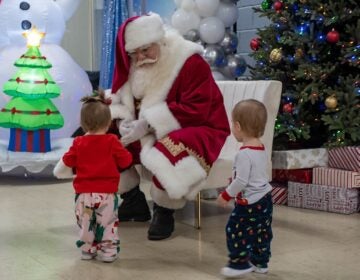 A person dressed as Santa greets two very young children