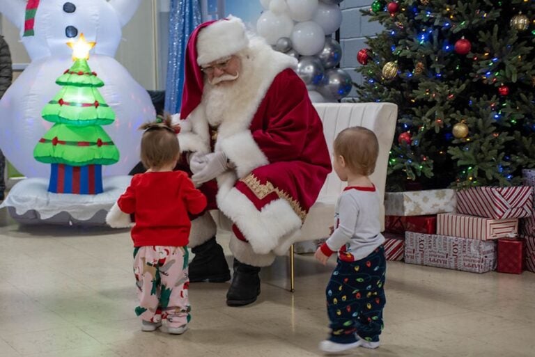 A person dressed as Santa greets two very young children