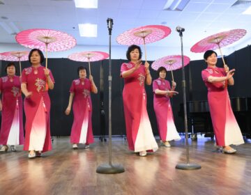 Asian women dance inside while holding traditional umbrellas
