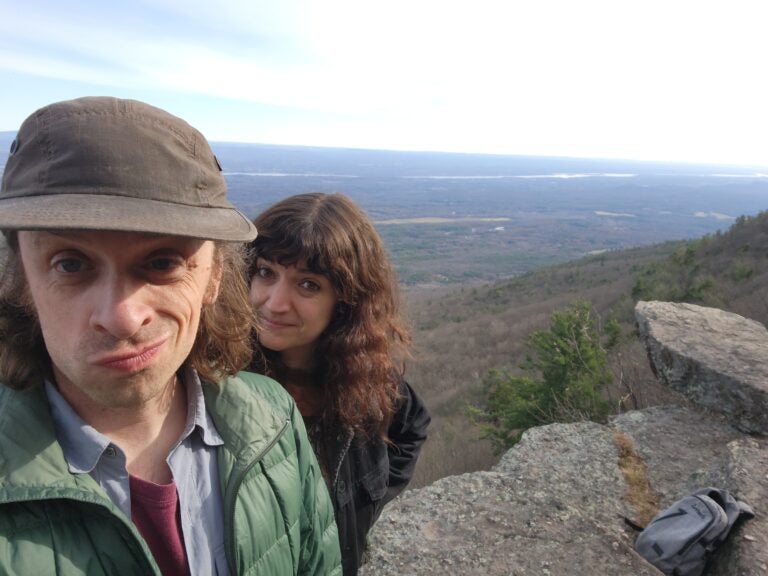 A selfie photo of Steve Heise and Alina Josan standing on a large hill overlooking a wide landscape