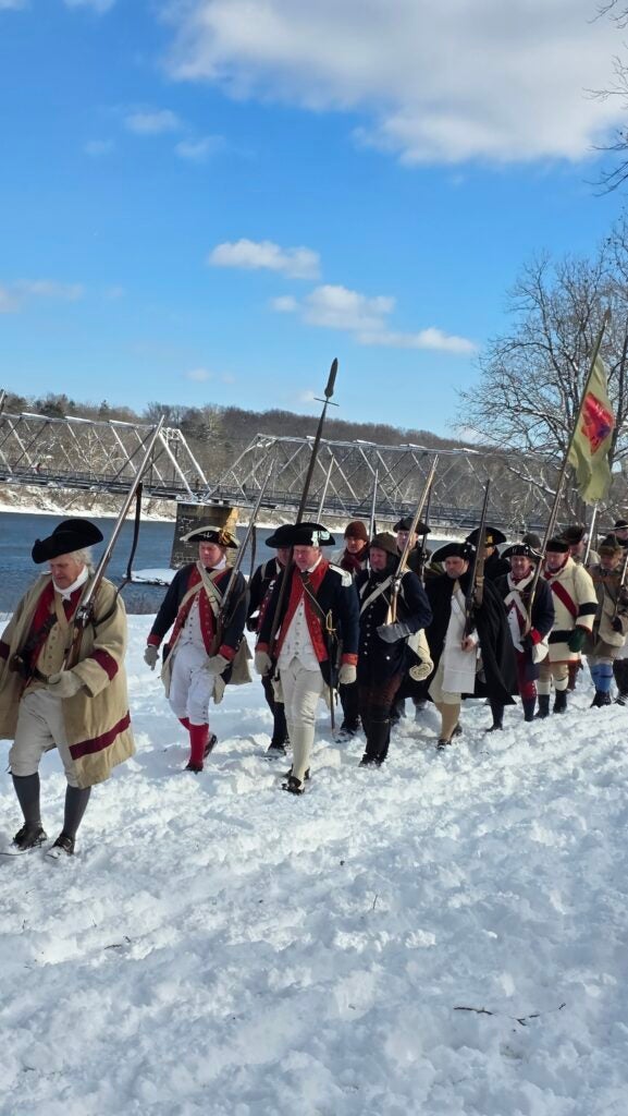 American Revolution reenactors march through the snow holding replica rifles from the era